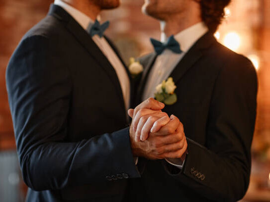 Close up of male gay couple dancing together during wedding ceremony and holding hands, copy space